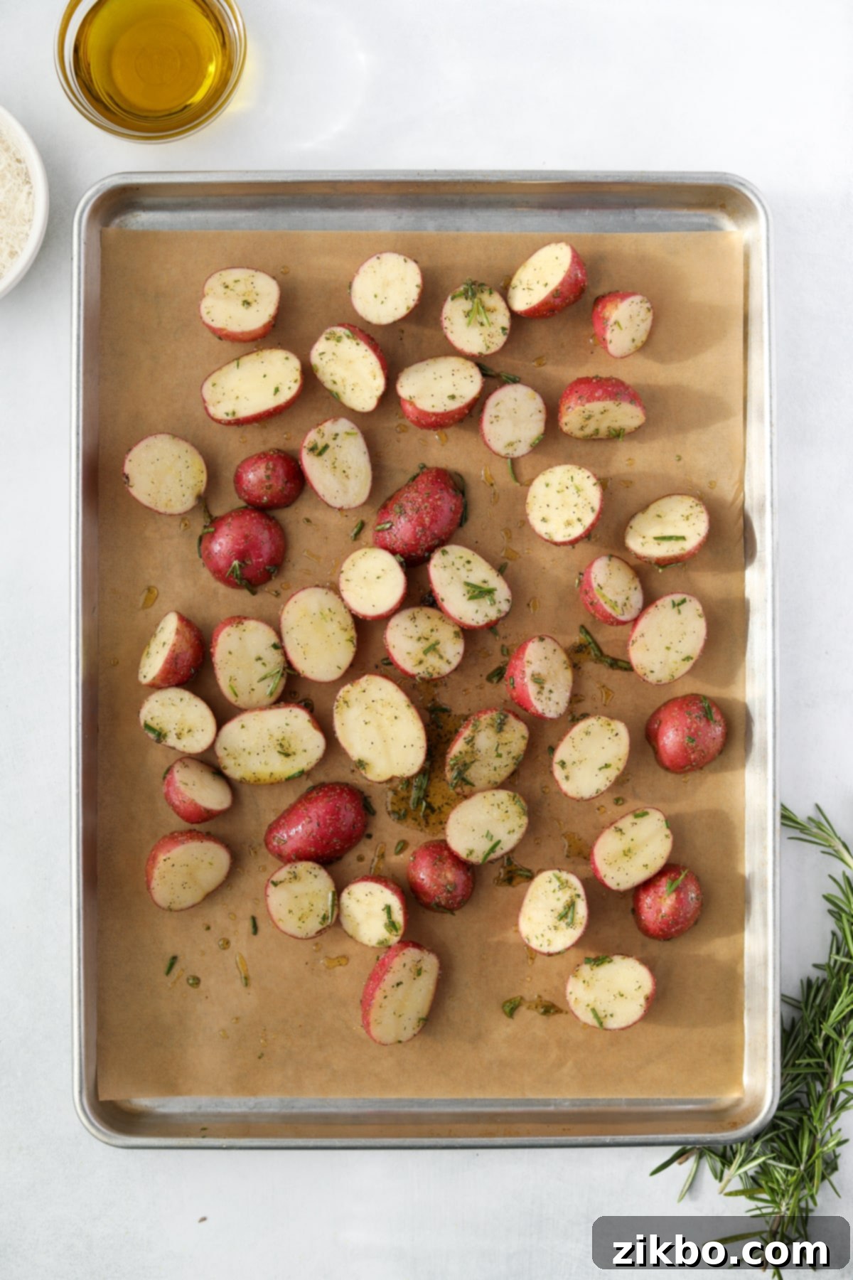 A baking sheet lined with parchment paper, topped with a single layer of potato halves spread out for optimal roasting.