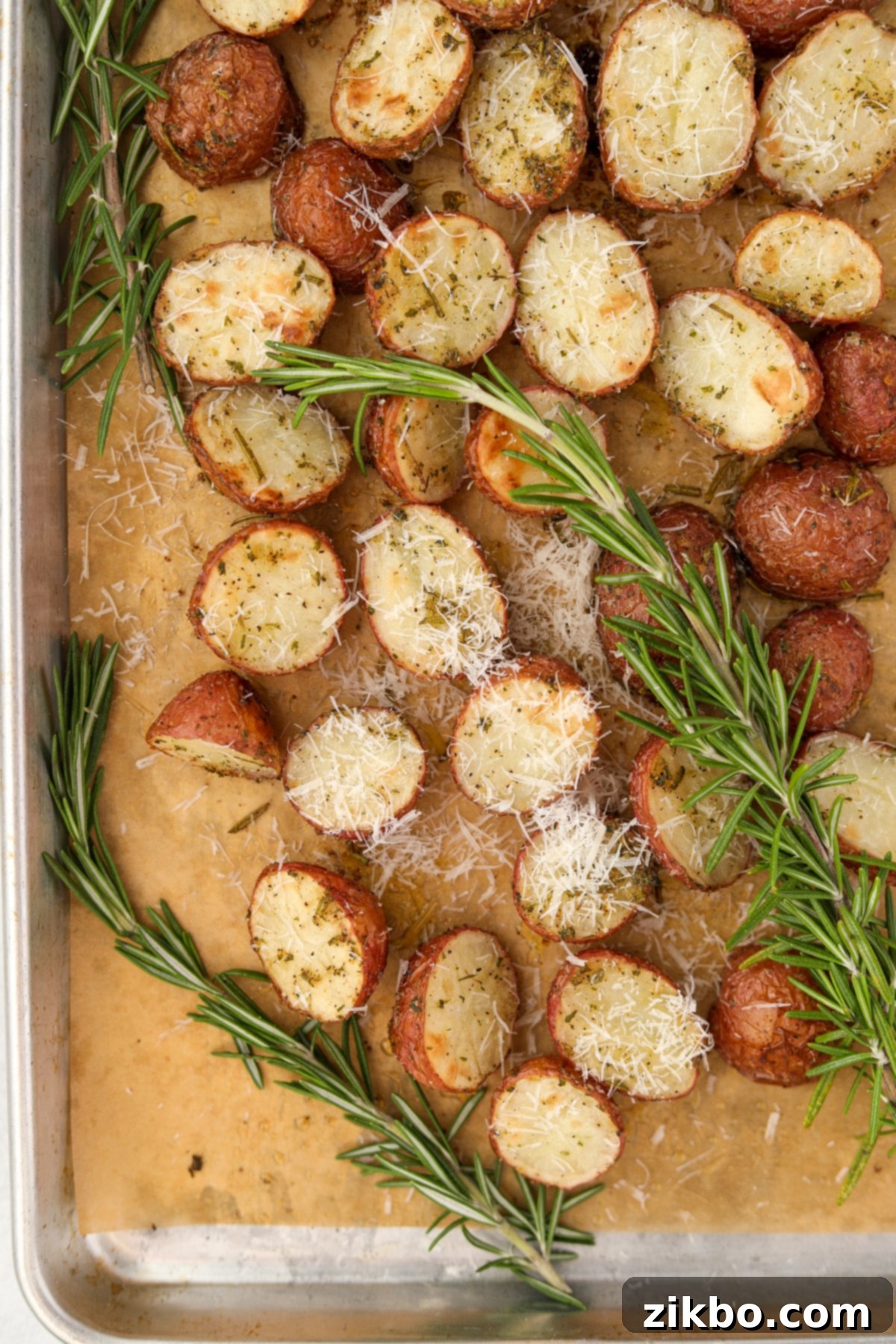 A sheet pan of roasted baby potatoes, freshly out of the oven, garnished with grated Parmesan cheese and fresh rosemary sprigs.