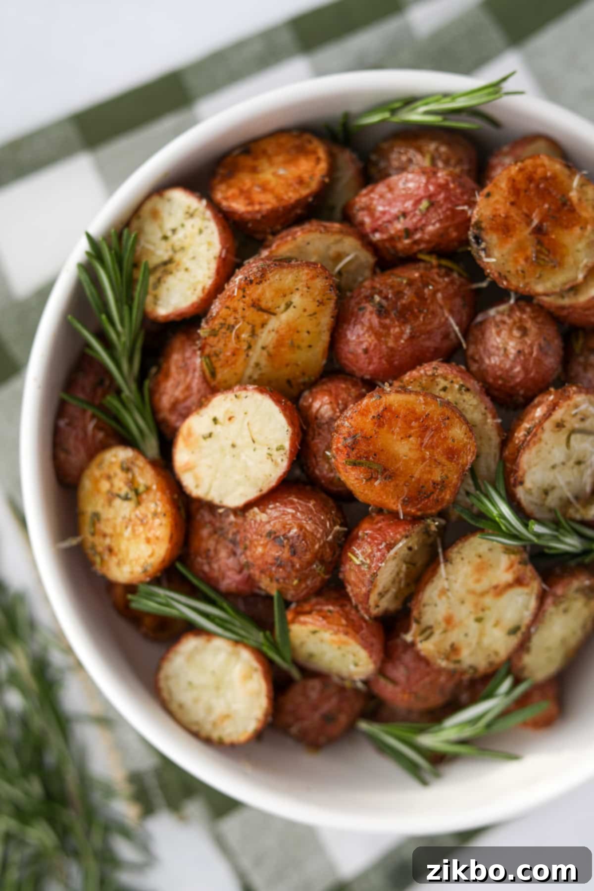 A rustic white bowl brimming with roasted rosemary potatoes, adorned with several sprigs of fresh rosemary for a fragrant garnish.