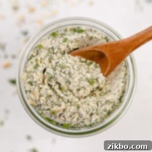 An overhead view of a jar of homemade ranch seasoning, with a small wooden spoon scooping some out.