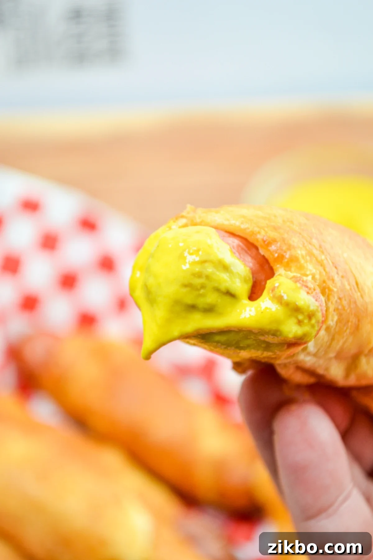 Crispy Air Fryer Pigs in a Blanket 3 A golden brown pig in a blanket, perfectly cooked and dipped in bright yellow mustard.