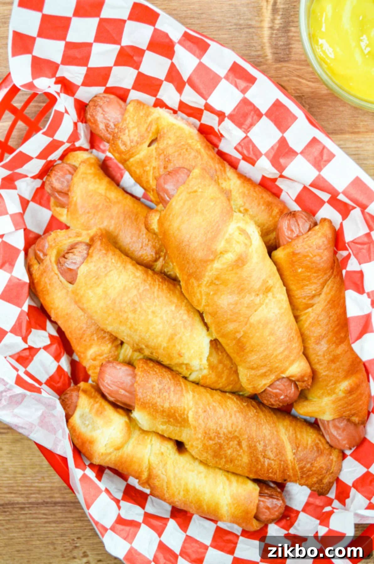 Crispy Air Fryer Pigs in a Blanket 9 A basket full of air-fried pigs in a blanket, accompanied by a small bowl of yellow mustard for dipping.