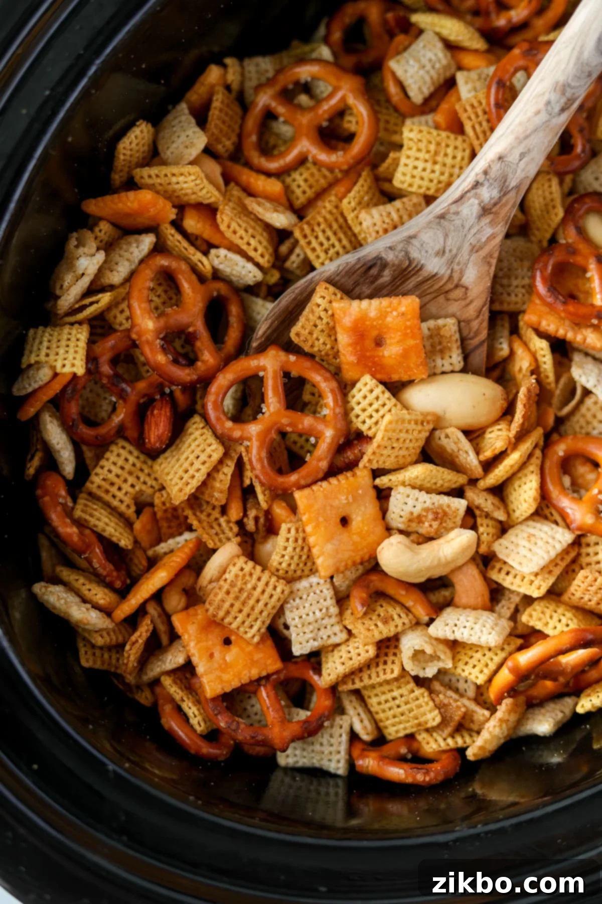 A wooden spoon scooping a generous portion of freshly made, golden brown Chex Mix from a slow cooker.