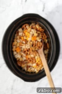 A wooden spoon stirring a crock pot full of Chex Mix.