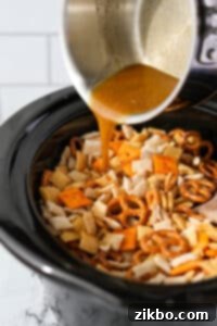 Pouring melted butter into a slow cooker filled with Chex Mix.