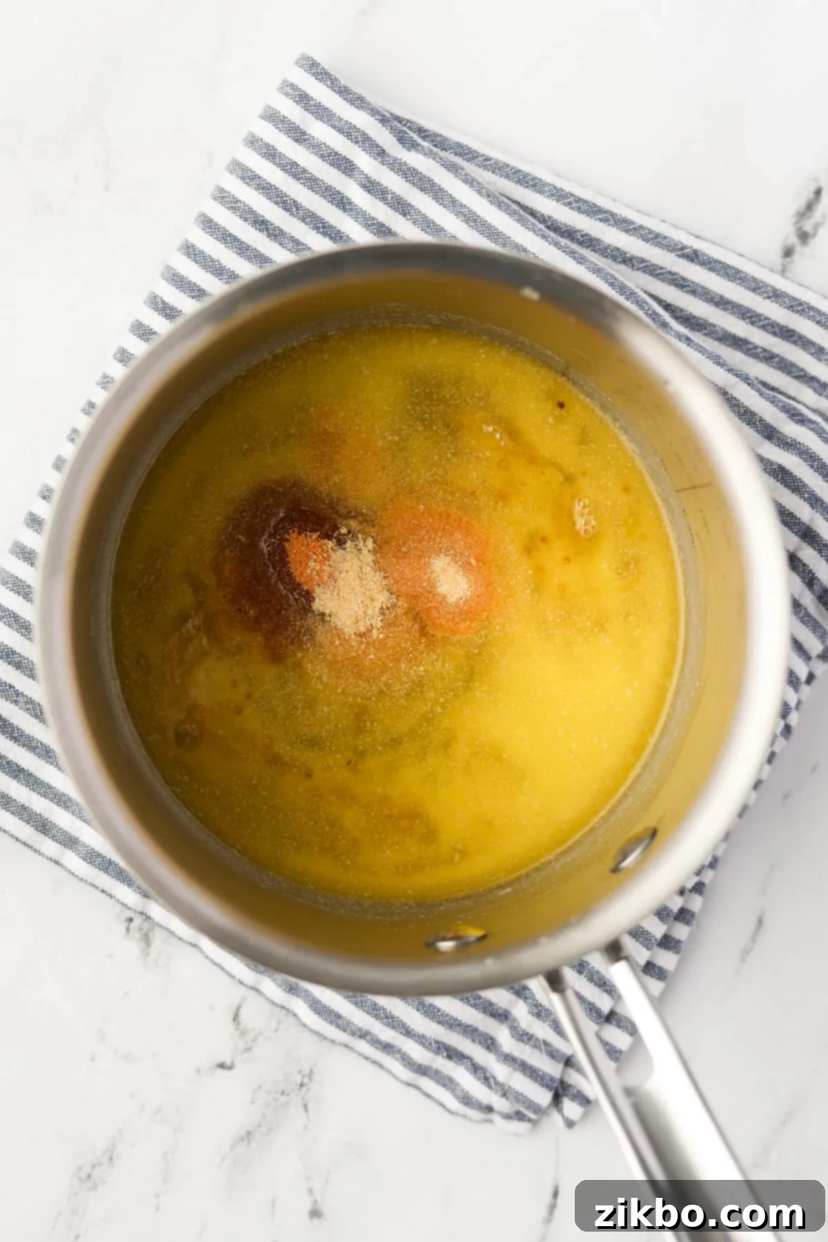 A small saucepan containing melted butter and various seasonings like garlic powder, onion powder, and seasoned salt, ready to be whisked.