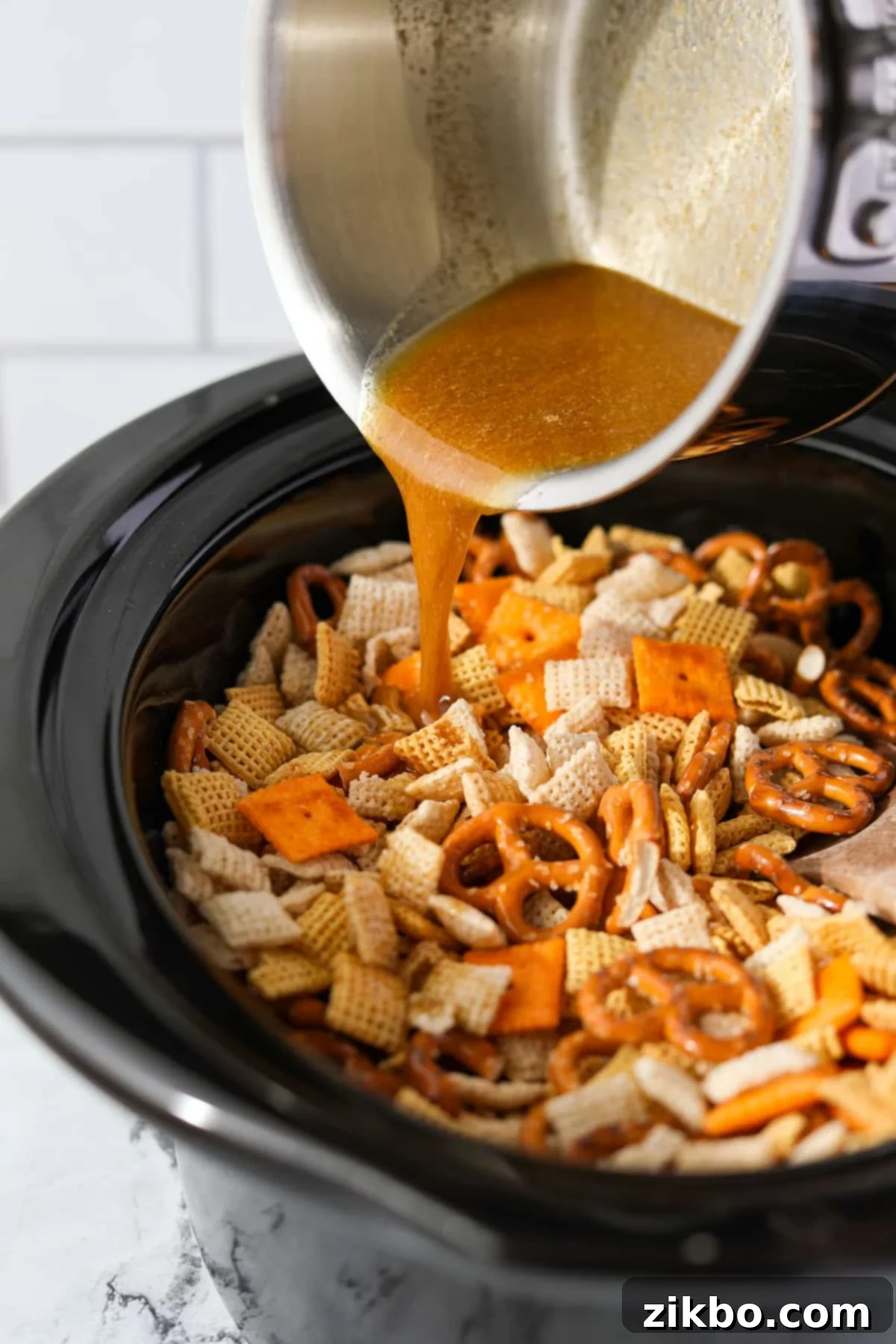 A stream of melted, seasoned butter being poured over the dry Chex Mix ingredients in a slow cooker.