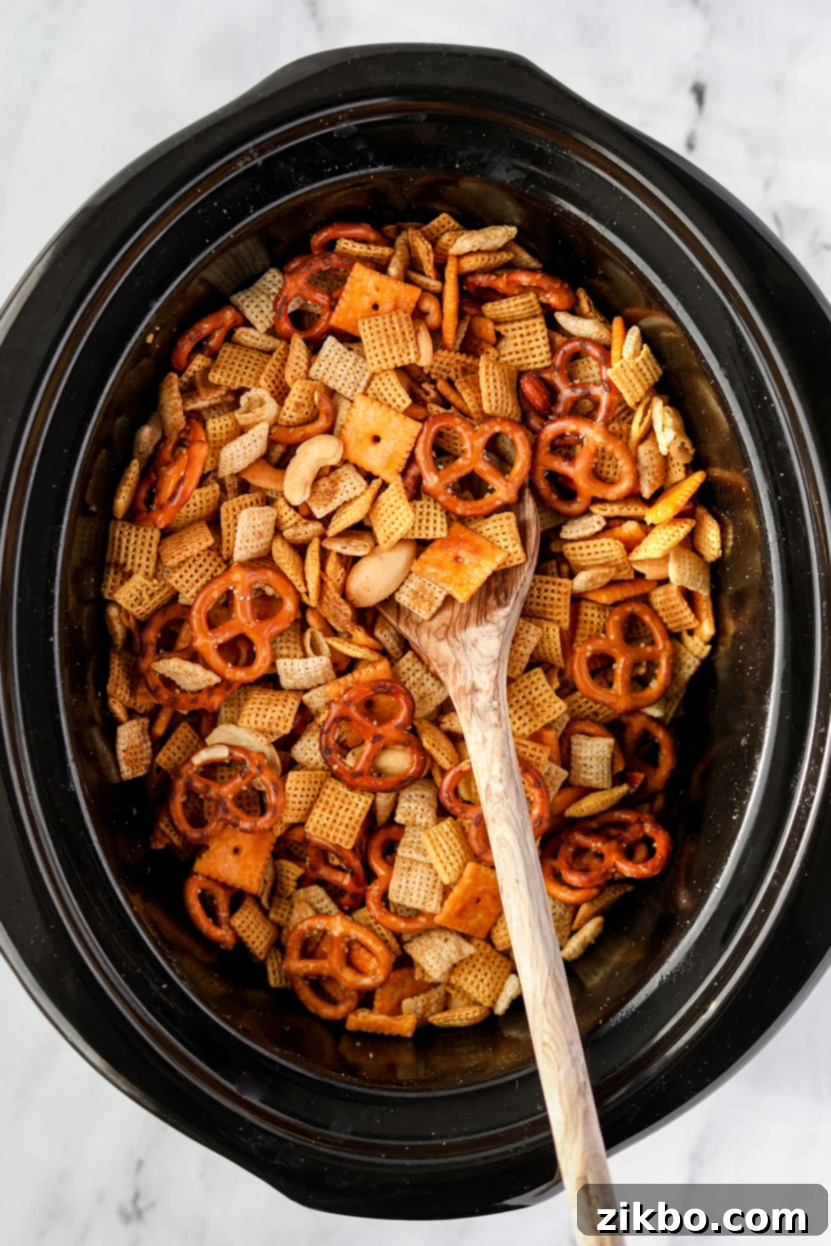 A close-up shot of Chex Mix being stirred in a slow cooker, showing the even coating of seasonings and butter.
