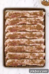 A baking sheet filled with bacon that has been sprinkled with brown sugar and spices.