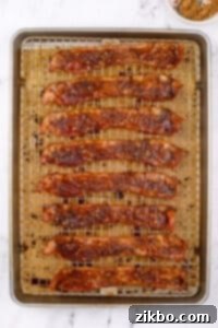 A baking sheet filled with cooked, crispy bacon coated with brown sugar, cooling on a wire rack.
