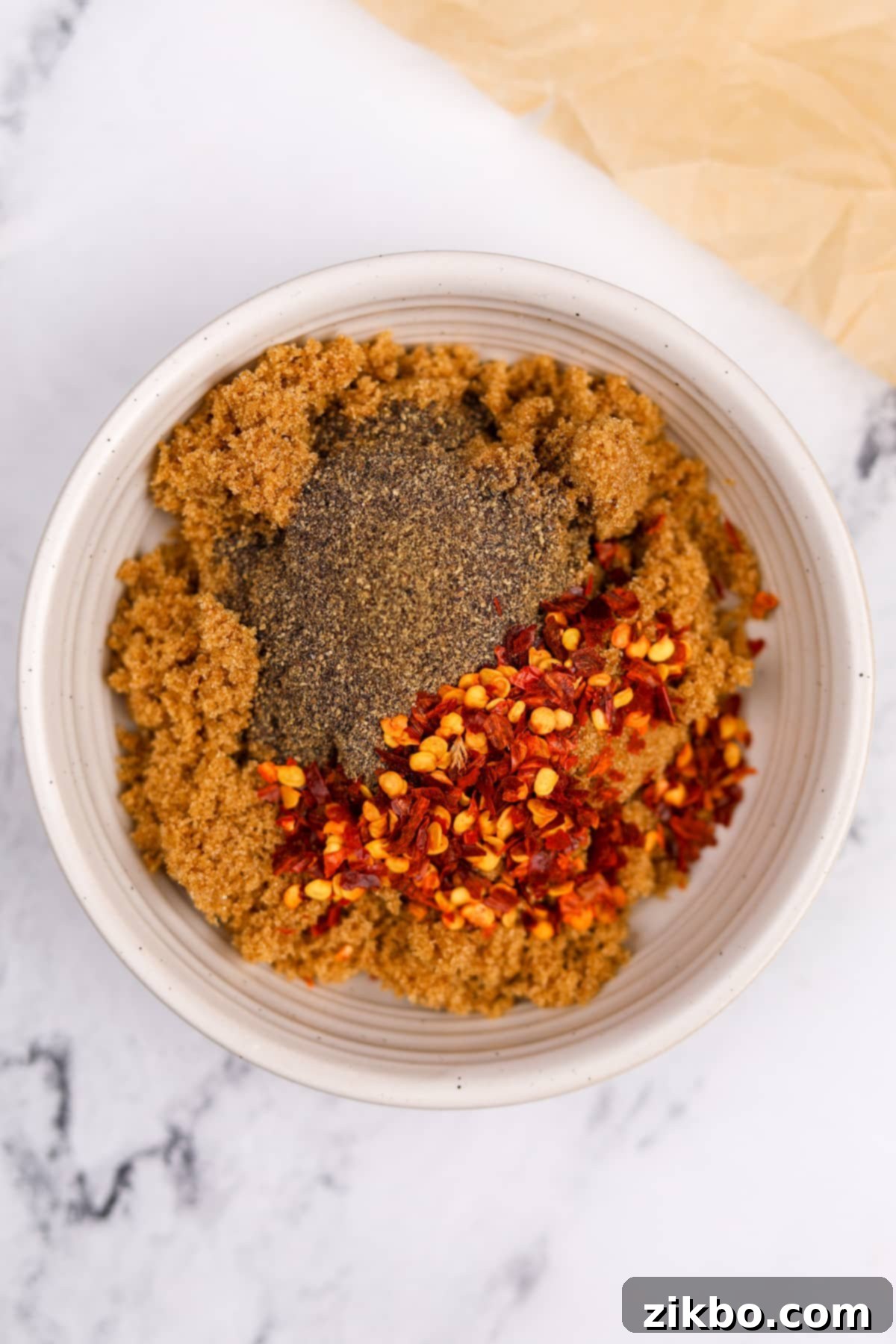 A small bowl with brown sugar, crushed red pepper flakes, and black pepper, ready to be mixed.