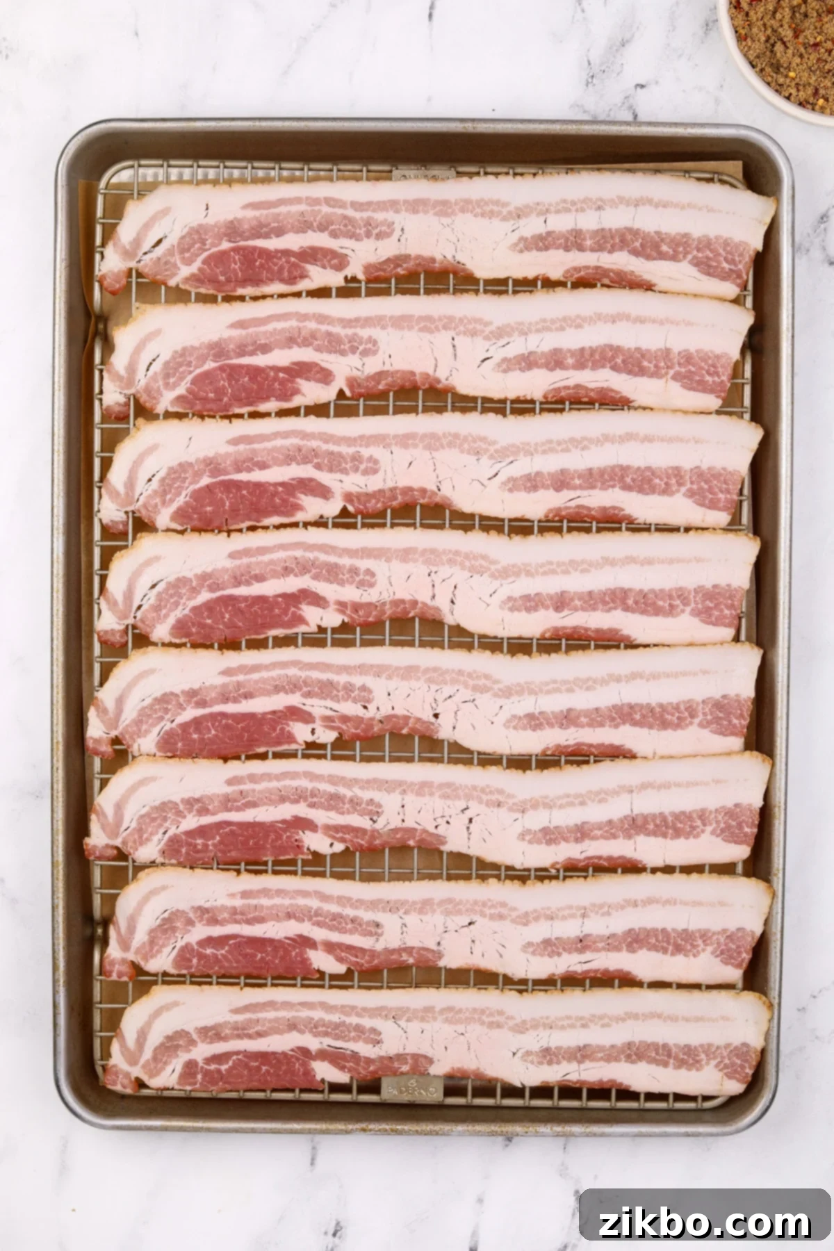 A baking sheet filled with evenly spaced bacon slices on a wire rack.