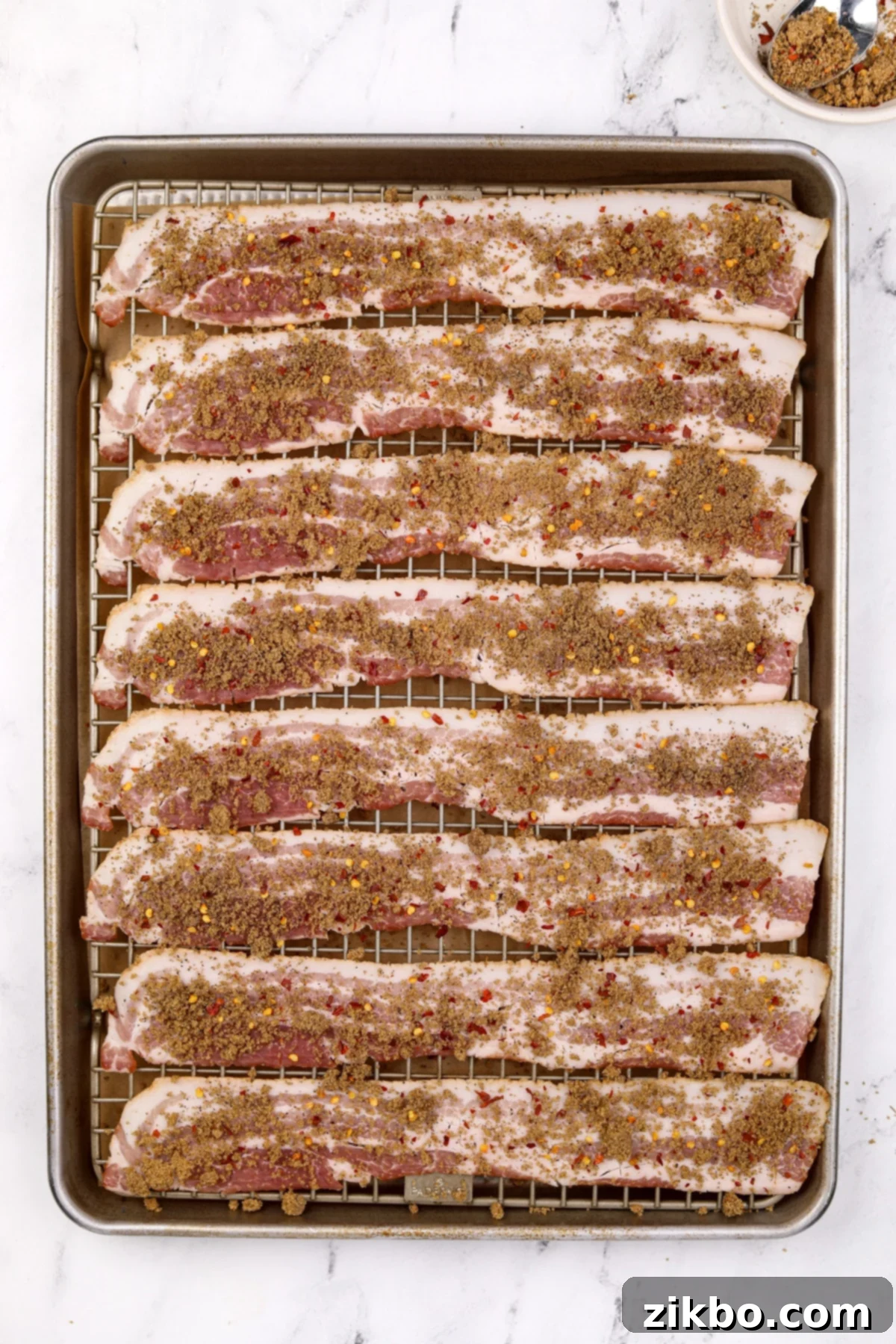 Bacon slices on a baking sheet, now sprinkled with the brown sugar and spice mixture.