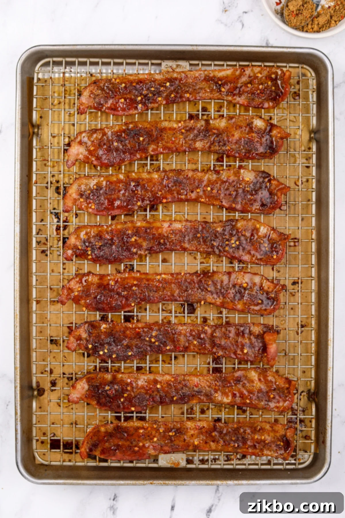 A baking sheet filled with cooked crispy bacon coated with brown sugar, cooling on a wire rack.
