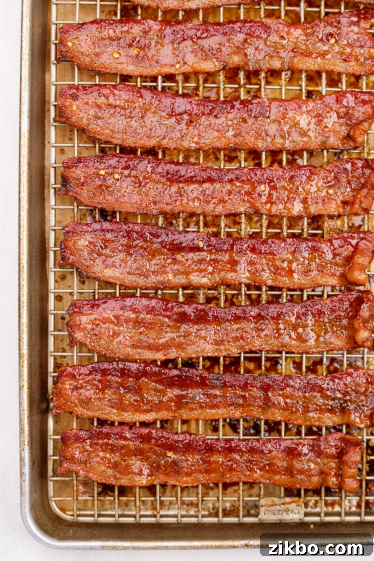 A baking sheet filled with a generous batch of cooked and beautifully candied Million Dollar Bacon slices, dotted with red pepper flakes.