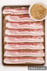 A baking sheet with bacon slices spread out on a wire rack, with a small bowl of brown sugar spice mix on the side.