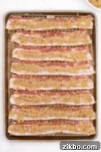 A baking sheet with bacon slices on a wire rack, generously topped with the brown sugar spice rub.