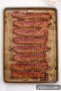 Perfectly cooked and candied bacon glistening on a baking sheet, cooling on a wire rack.