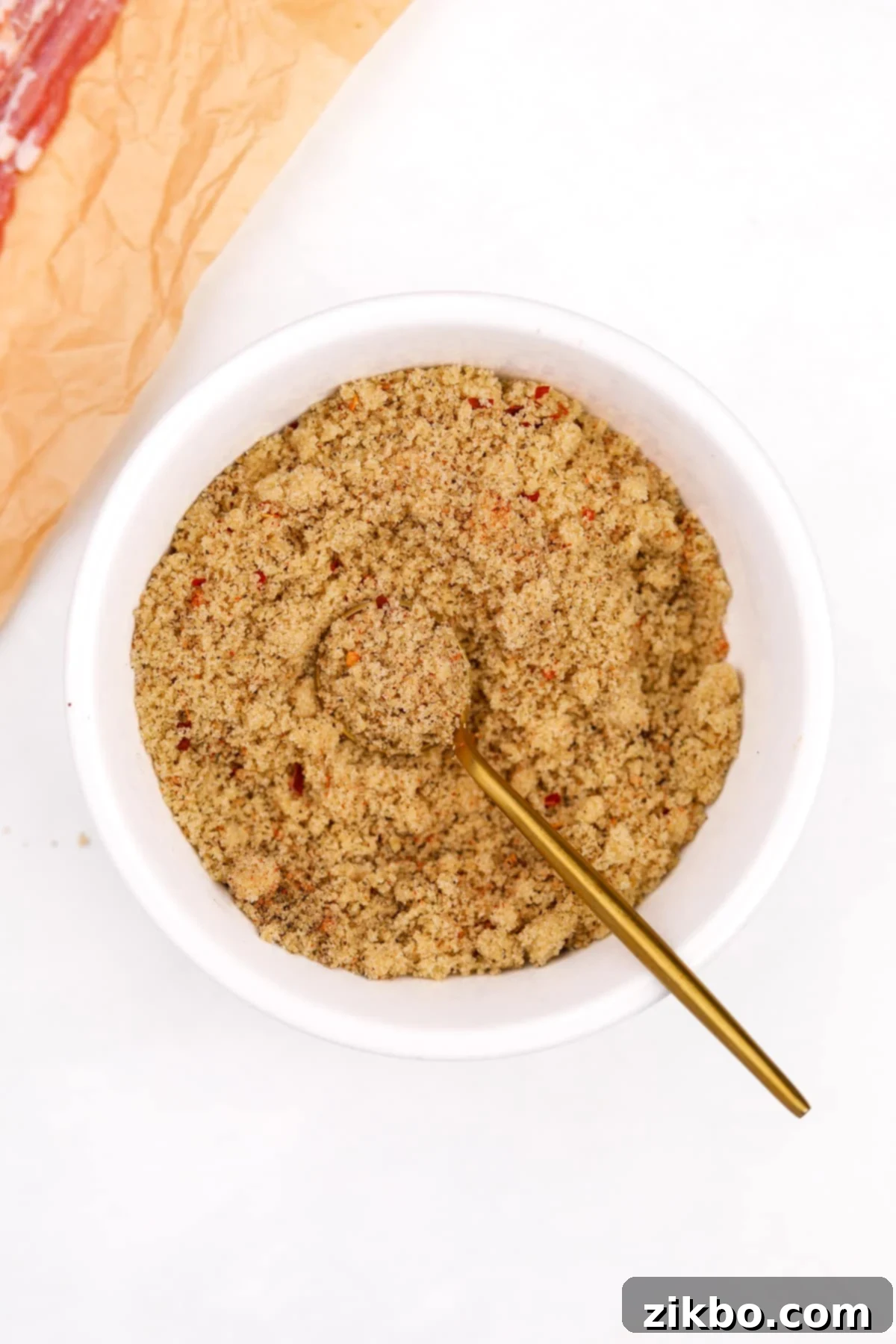 A small bowl containing the well-mixed brown sugar and spice rub with a gold spoon.