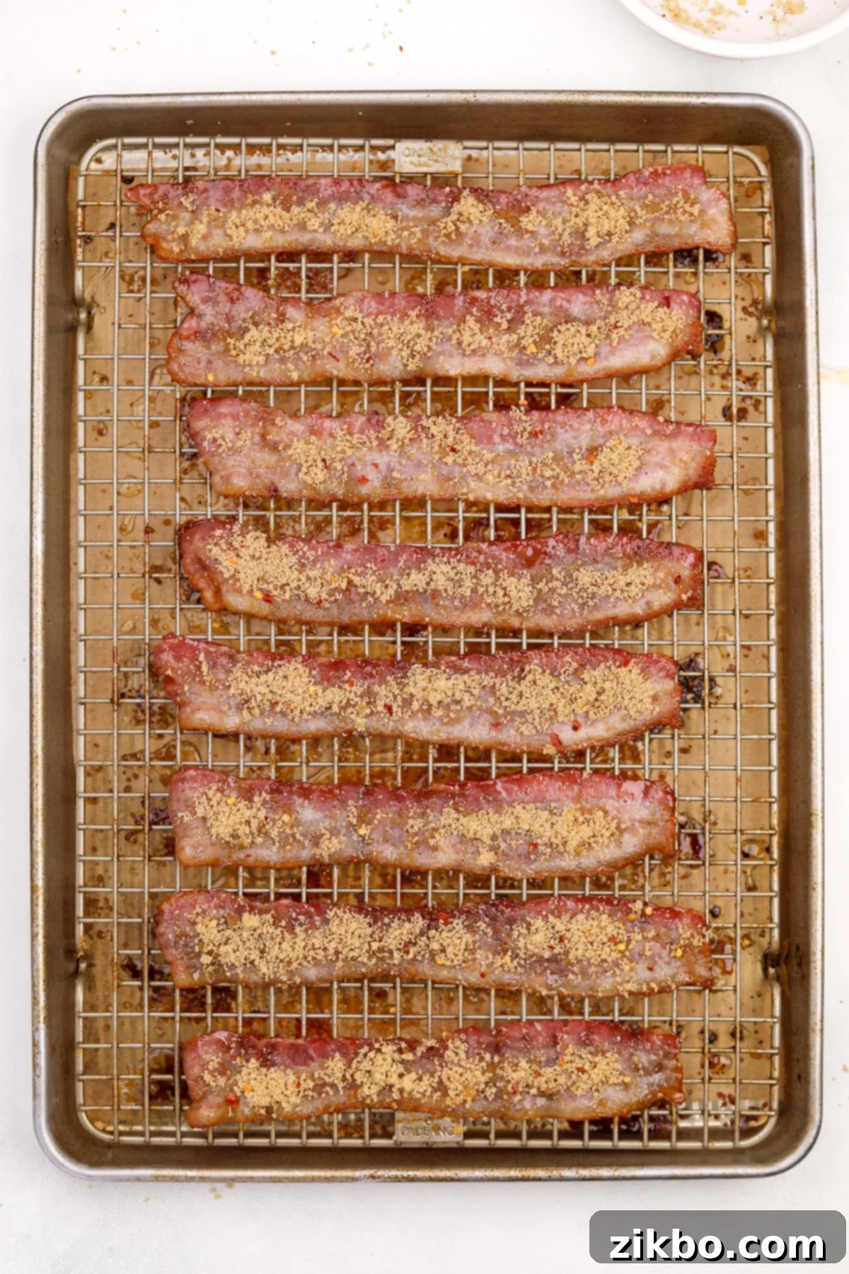 Bacon slices on a baking sheet, now flipped over and ready for the remaining brown sugar mixture.