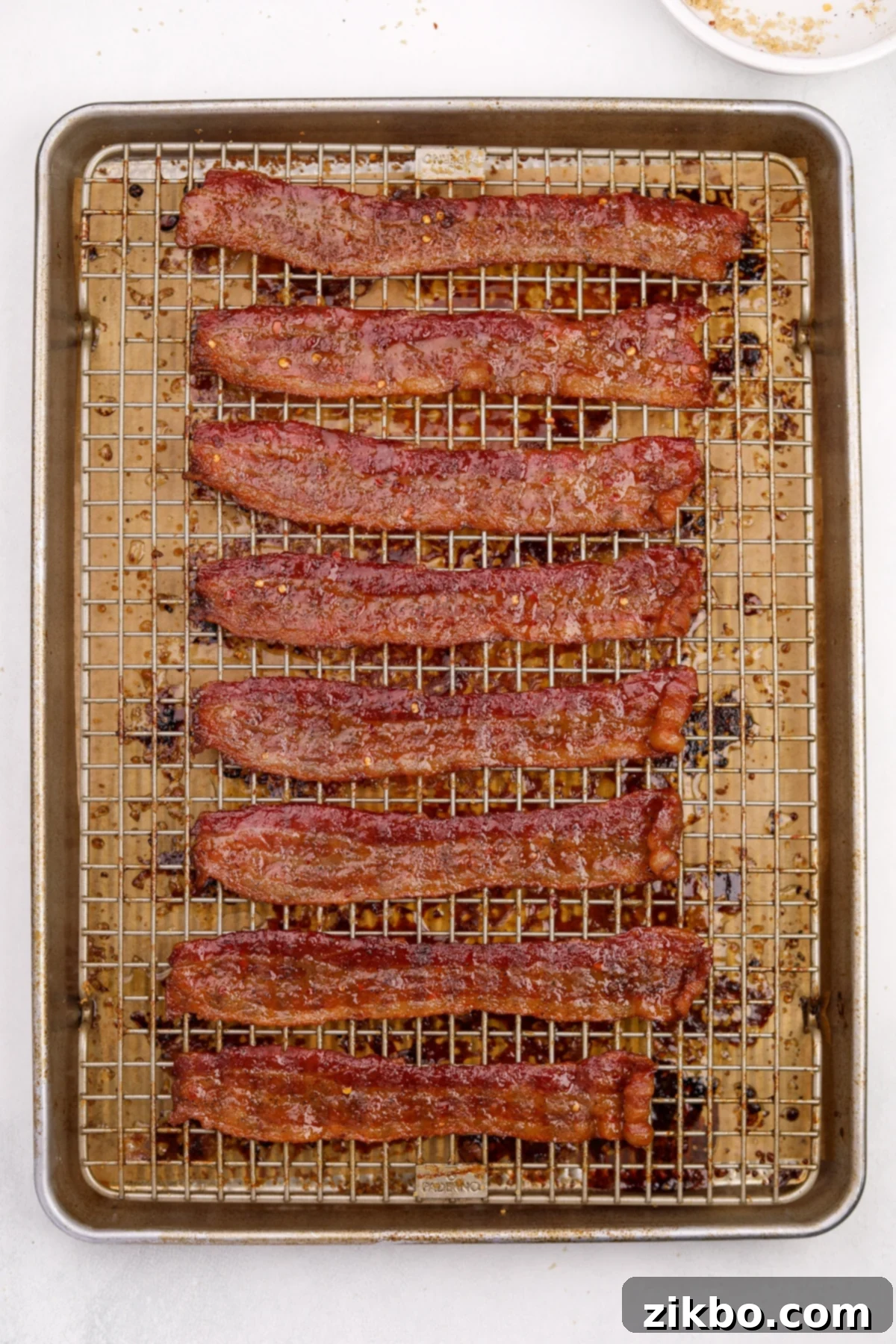 Perfectly cooked and candied bacon glistening on a baking sheet, ready to be served.