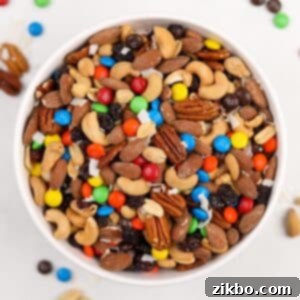 A white bowl filled with homemade trail mix, featuring nuts, raisins, and M&M's.