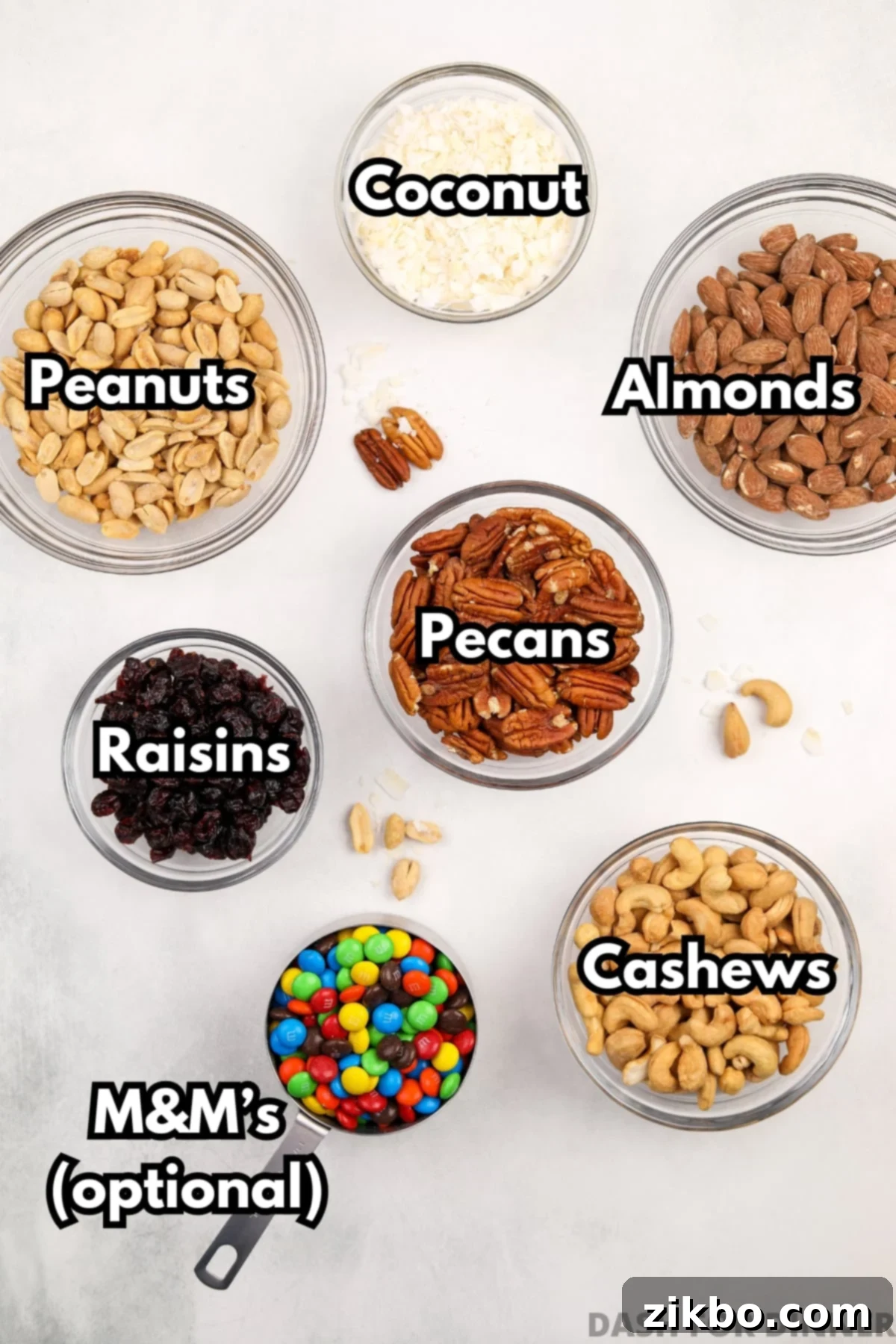 The array of core ingredients laid out for making homemade trail mix: pecans, almonds, cashews, raisins, coconut flakes, and colorful M&M's.