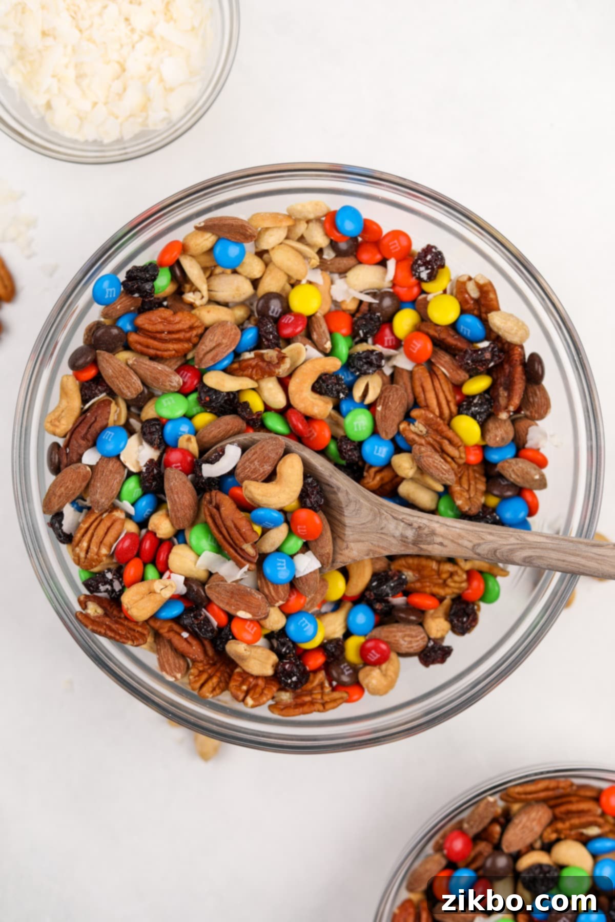 A large bowl filled with freshly made trail mix, featuring a mix of nuts, dried fruit, and colorful M&M's candies, ready to be stored or served.