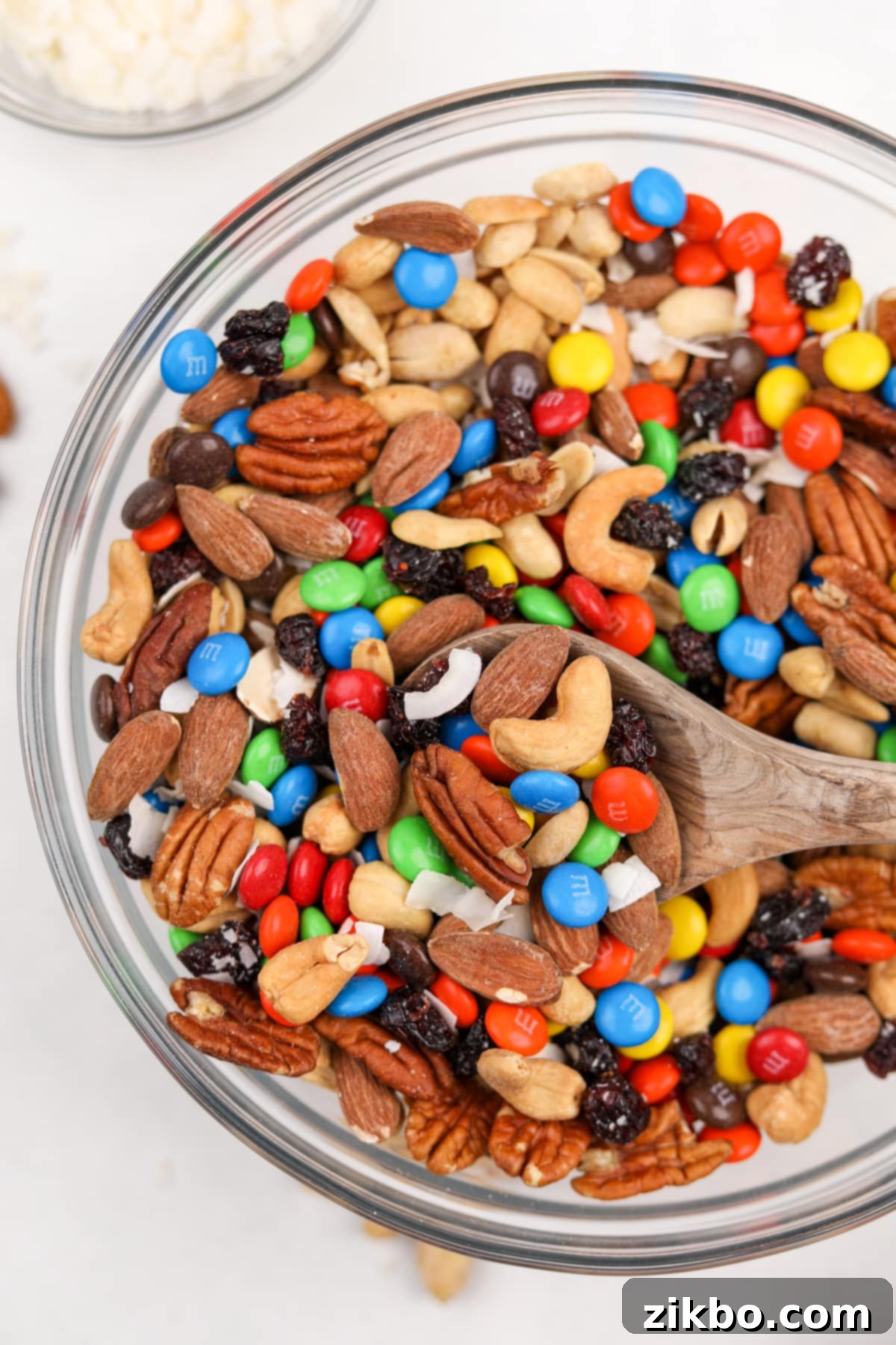 A large bowl of homemade trail mix being scooped with a wooden spoon, ready for serving or packing.