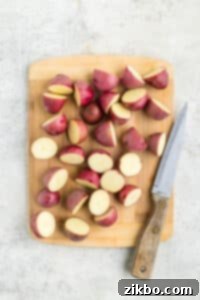 Slicing baby red potatoes into halves on a wooden cutting board, ensuring uniform pieces for even cooking.
