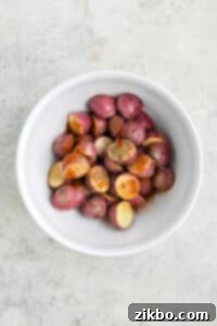 A large bowl of cut red potatoes generously topped with olive oil and a savory blend of seasonings, ready for tossing.