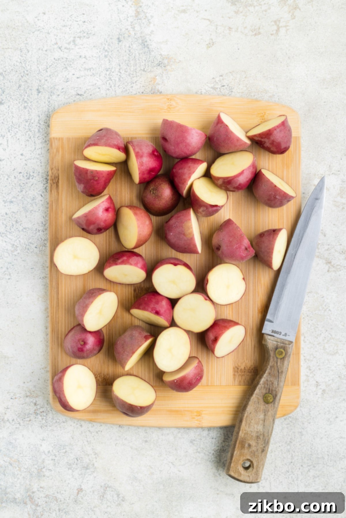 Slicing baby red potatoes into halves on a wooden cutting board.