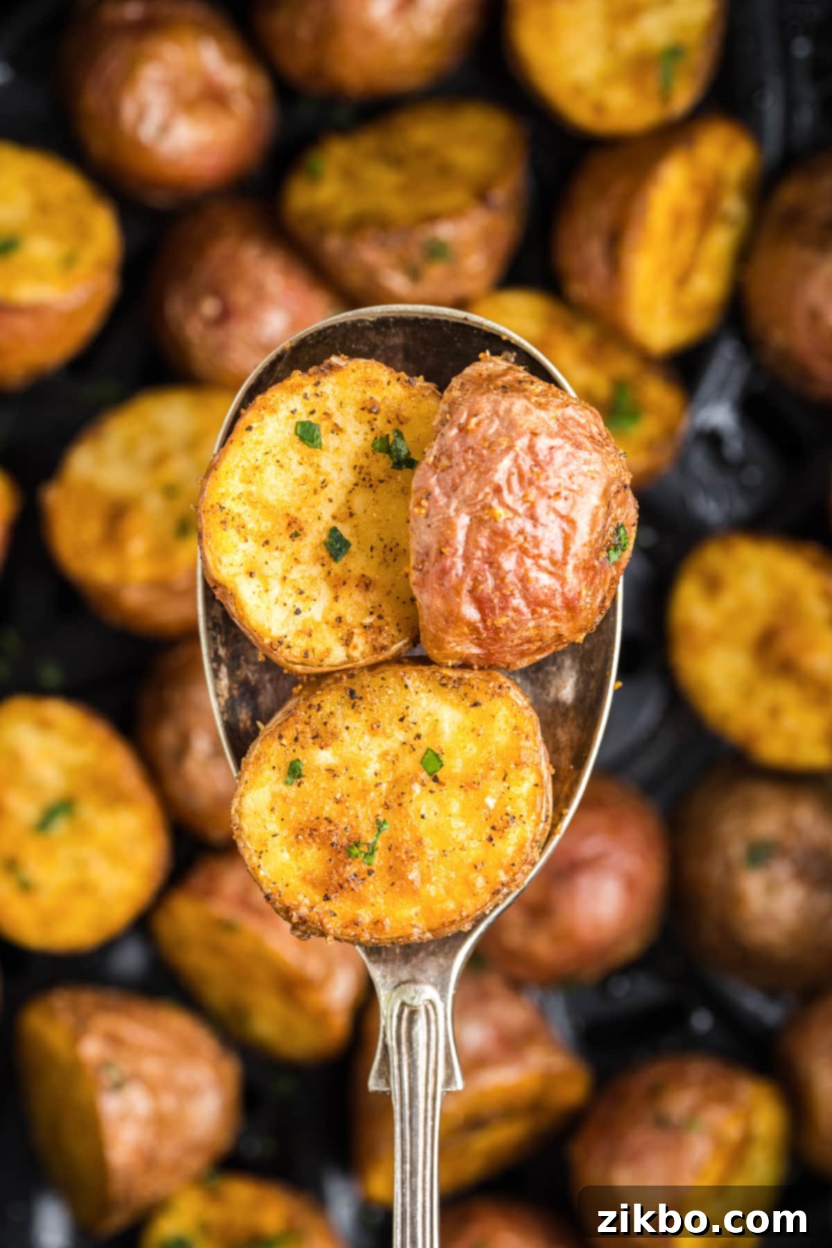 A large serving spoon scooping roasted red potato halves, glistening with seasoning.