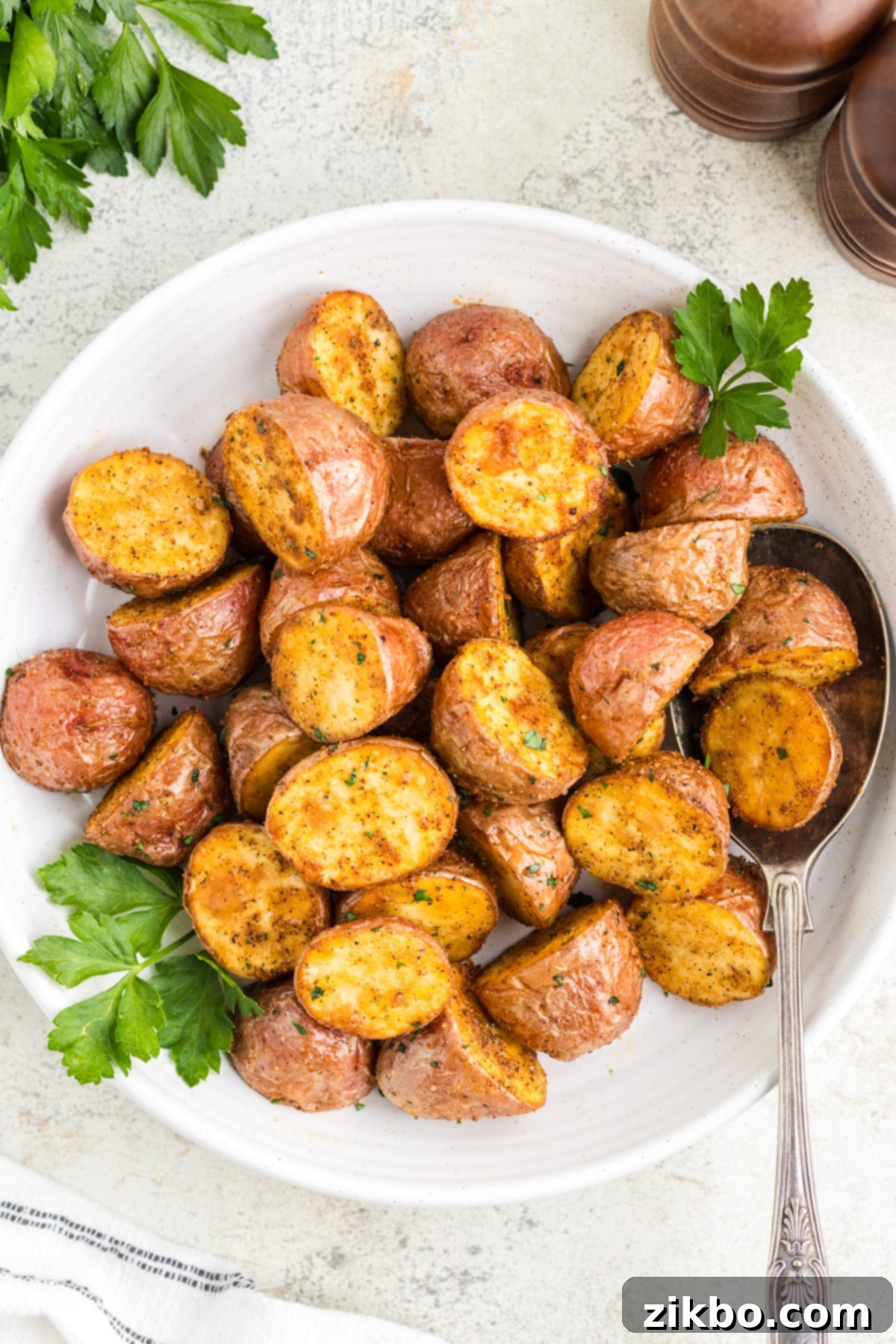 A white plate filled with perfectly roasted red potatoes, garnished with fresh parsley.