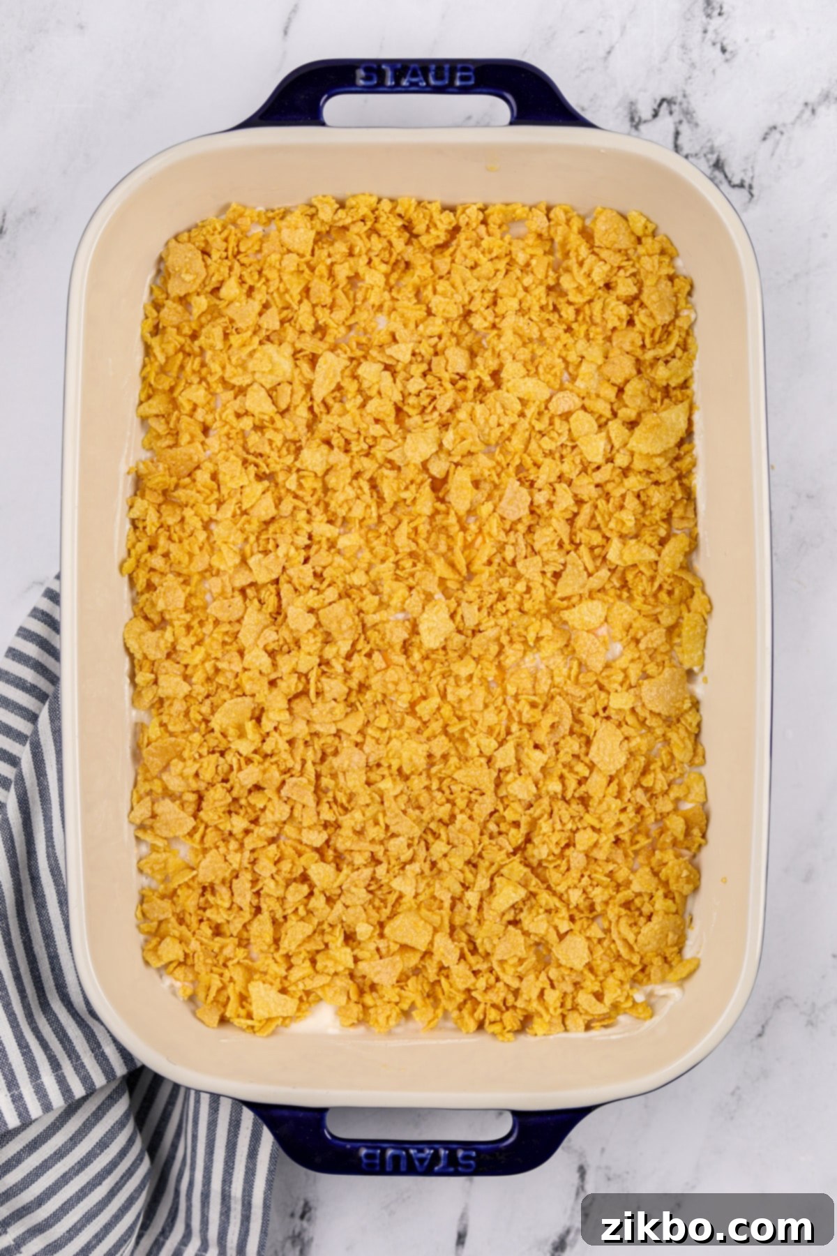 A baking dish filled with potato casserole, topped generously with the buttery corn flake mixture, ready for the oven.