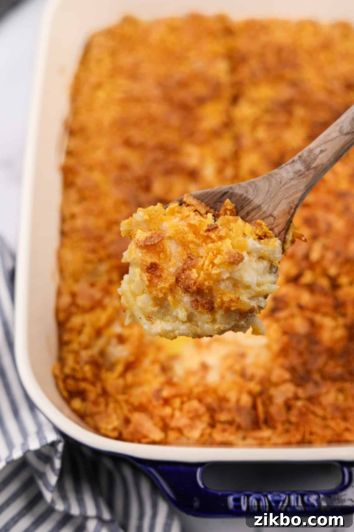 A scoop of golden-brown hash brown casserole, displaying its cheesy interior and crispy top, just out of the baking dish.