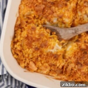 A wooden spoon scooping from a baking dish of hash brown casserole, showing its golden-brown topping and creamy interior.