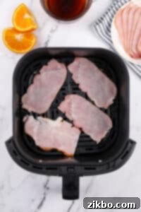 An air fryer basket with canadian bacon slices inisde.