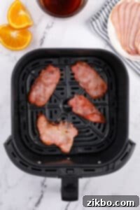 An air fryer basket with four slices of cooked back bacon inside.