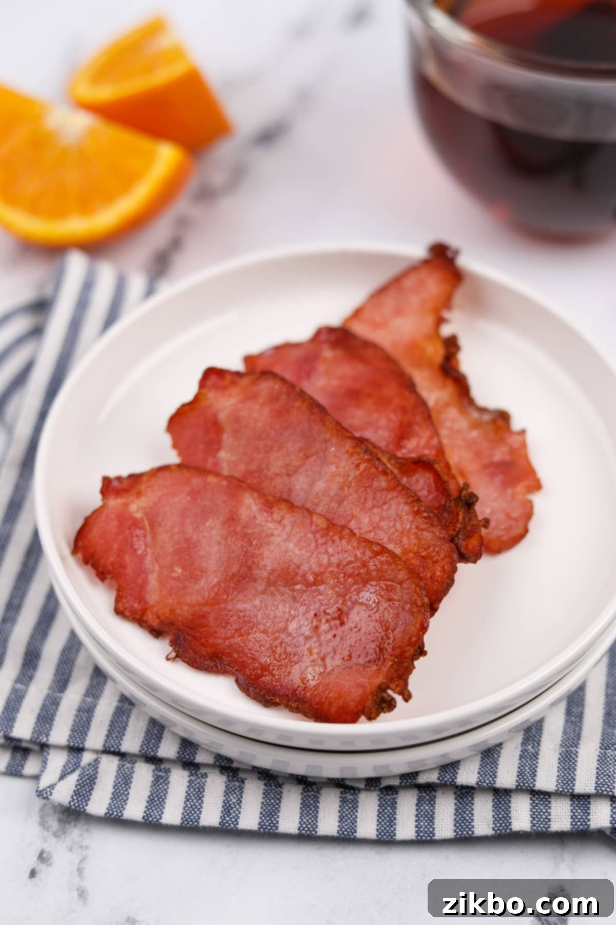 A white plate resting on a striped napkin with four slices of cooked Canadian bacon.