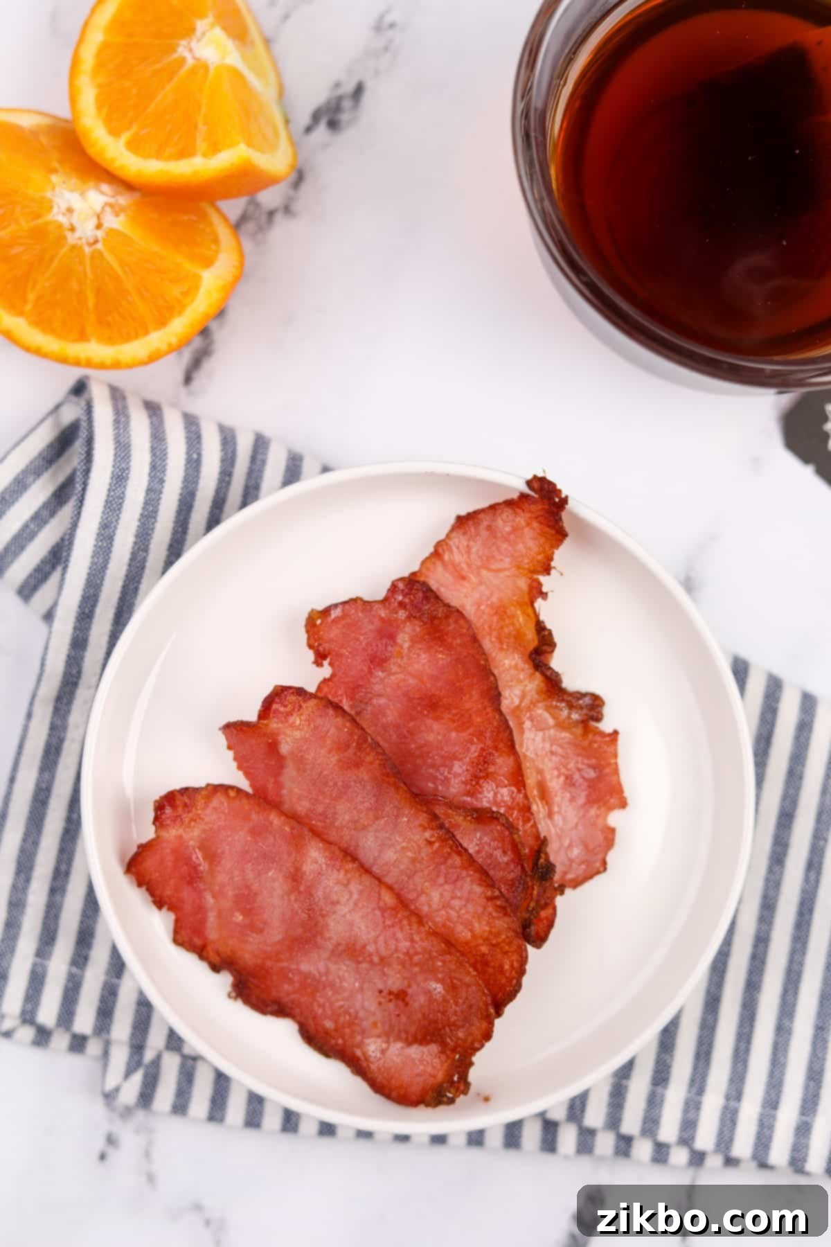 A white plate with four cooked slices of back bacon, ready to serve.