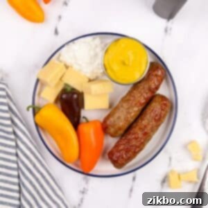 A plate filled with an appetizing arrangement of air fryer chicken sausages, fresh green vegetables, creamy cottage cheese, and a dollop of mustard.